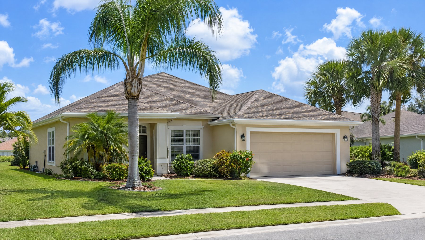 Single-story Florida home with a weathered wood colored architectural shingle hip roof, a green lawn and palms