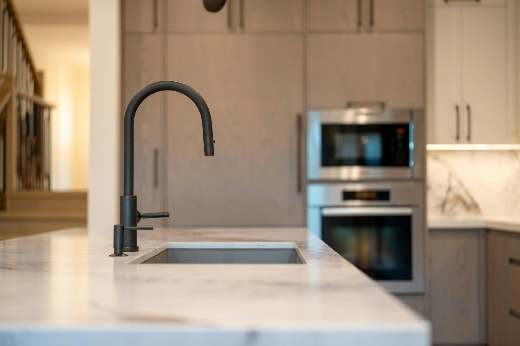 Matte black pull-down faucet on a marble kitchen island with wood cabinets and wall ovens behind