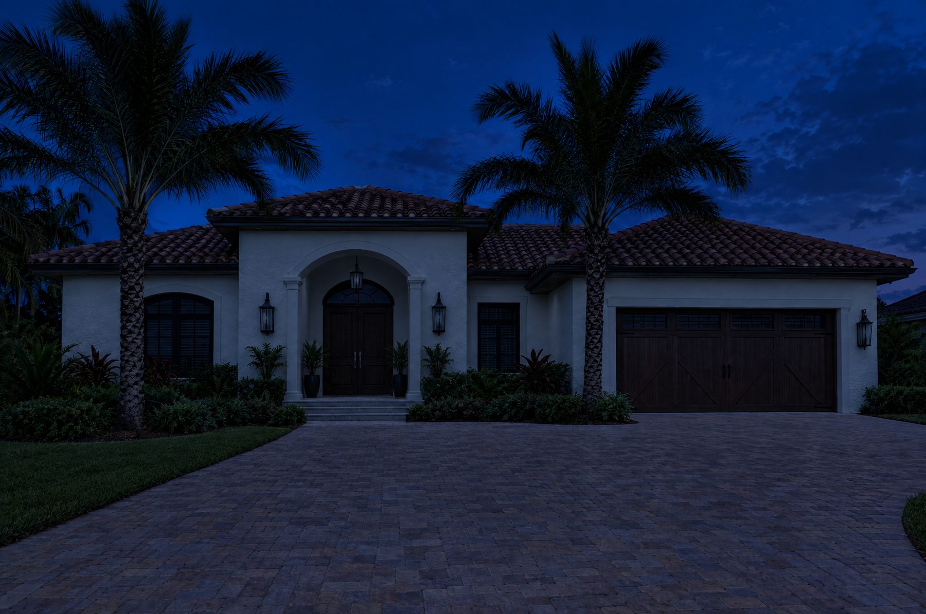 A Spanish style Florida home with a barrel tile roof at night, its lanterns, soffit lights and palm uplights switching on as motion is detected