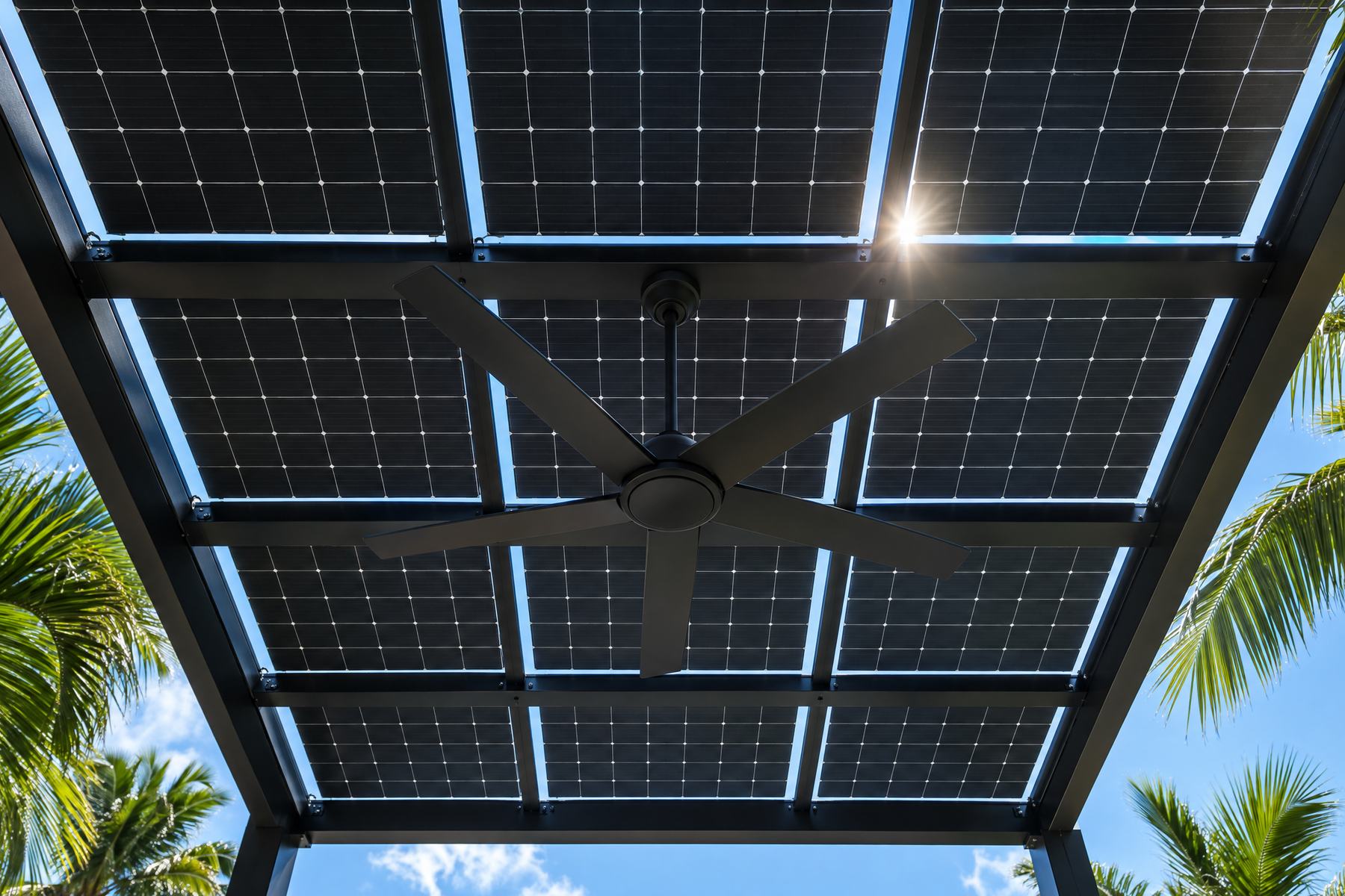 Looking up from under a solar pergola at the grid of all-black panels between black aluminum rafters, with thin lines of sky and a ceiling fan