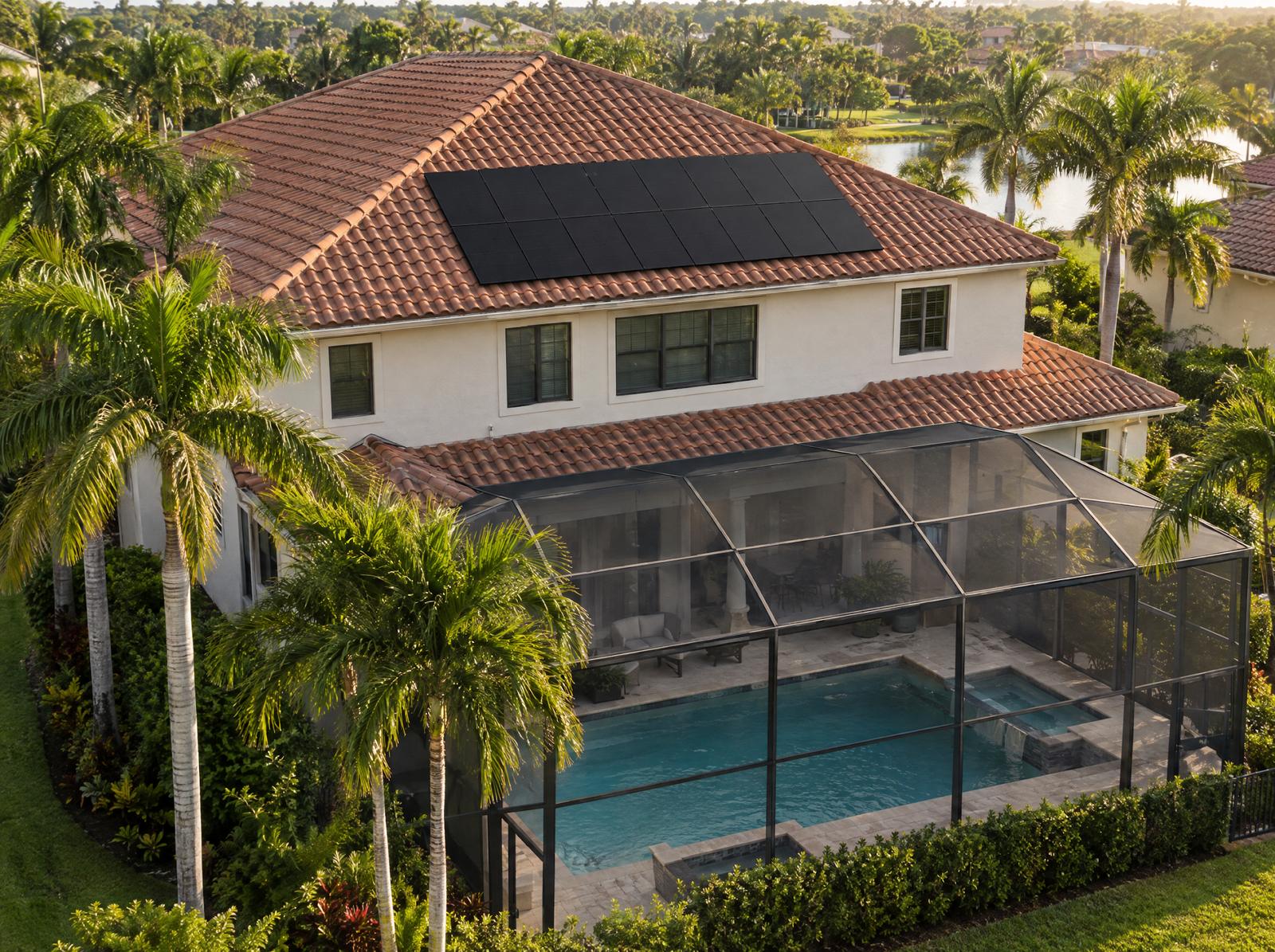 A two-story Mediterranean style Florida home with all-black solar panels on a terracotta tile roof above a screened pool